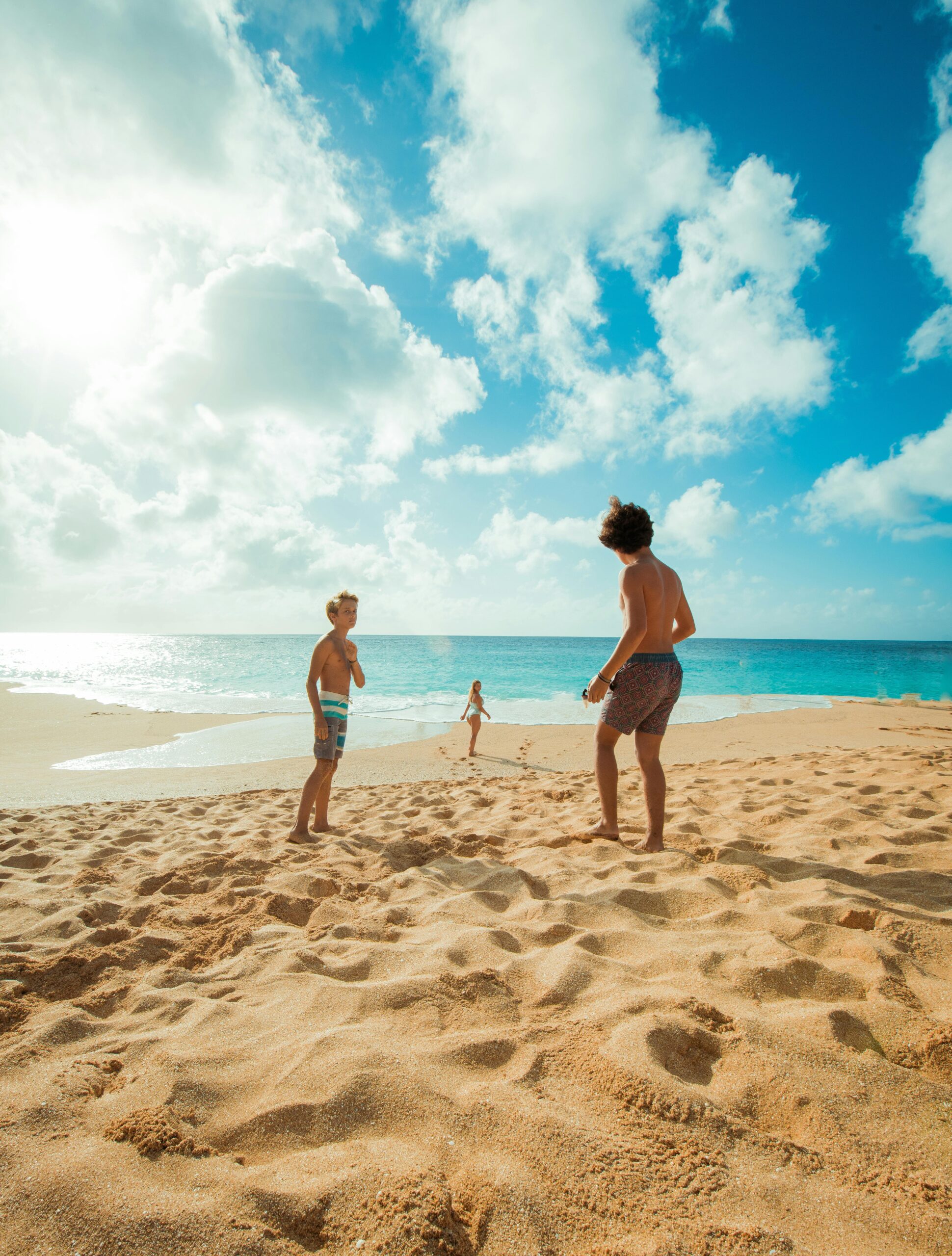 Three children enjoy a sunny day playing on Waialua Beach, Hawaii, with clear skies and blue ocean waters.