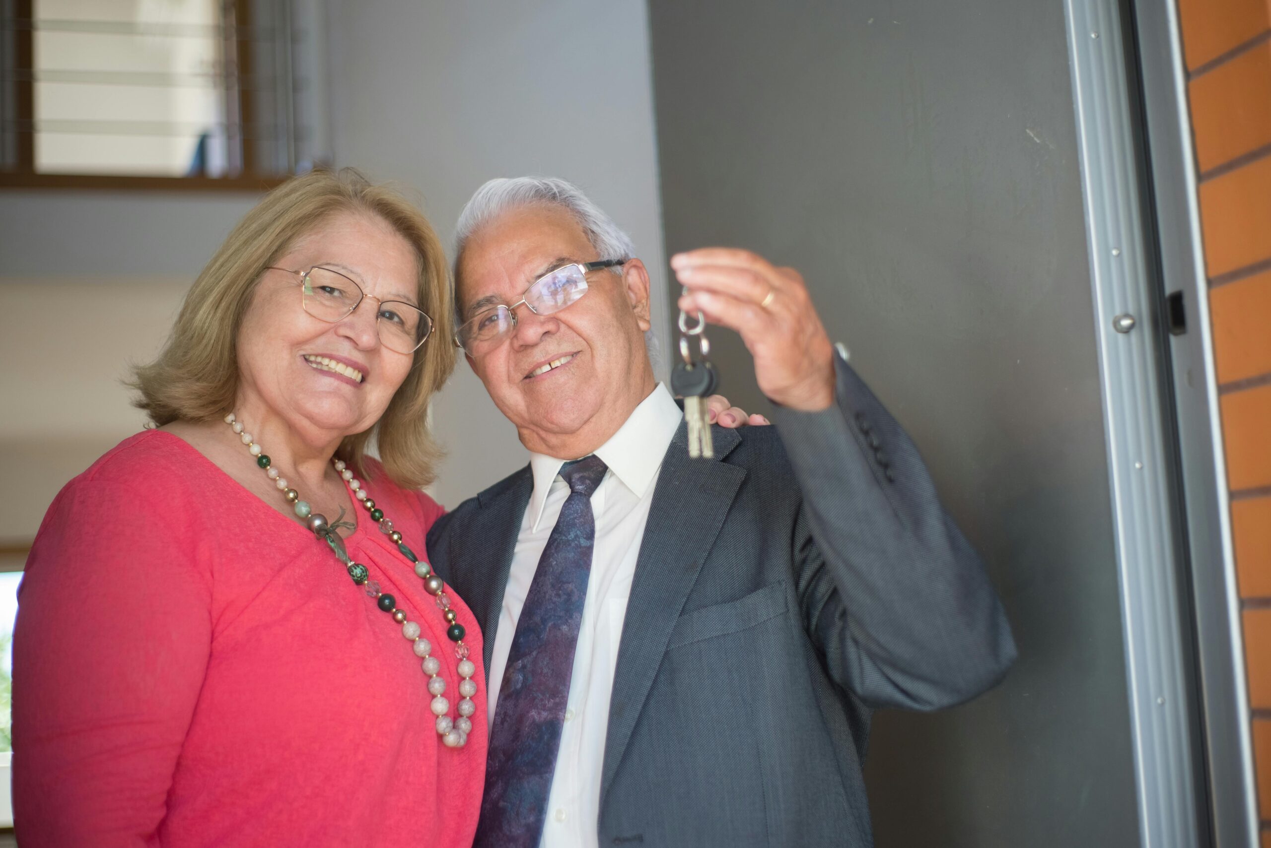Elderly couple happily holding keys, symbolizing new homeownership.